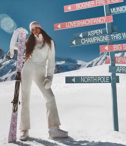 Mulher com look branco de neve segurando esquis nas montanhas